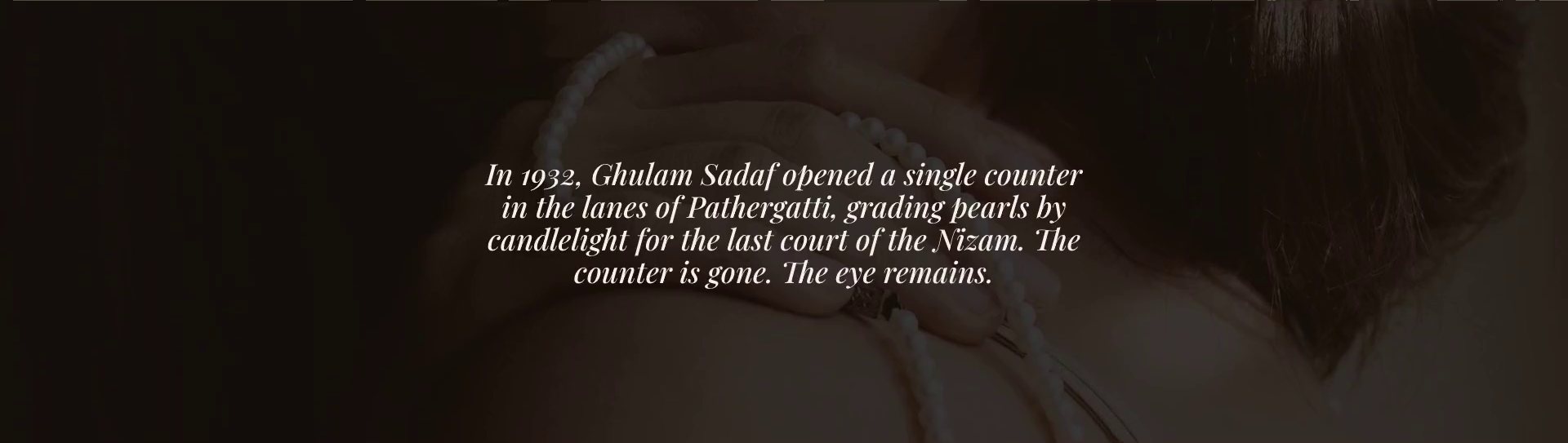 SADAF's heritage band: a dark photograph of a woman's hand resting on a pearl strand at her shoulder, behind the italic lines: In 1932, Ghulam Sadaf opened a single counter in the lanes of Pathergatti, grading pearls by candlelight for the last court of the Nizam. The counter is gone. The eye remains.